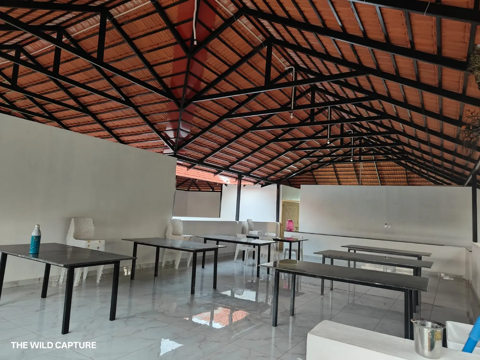 Open dining hall under an exposed truss and terracotta tile roof, with long tables and benches