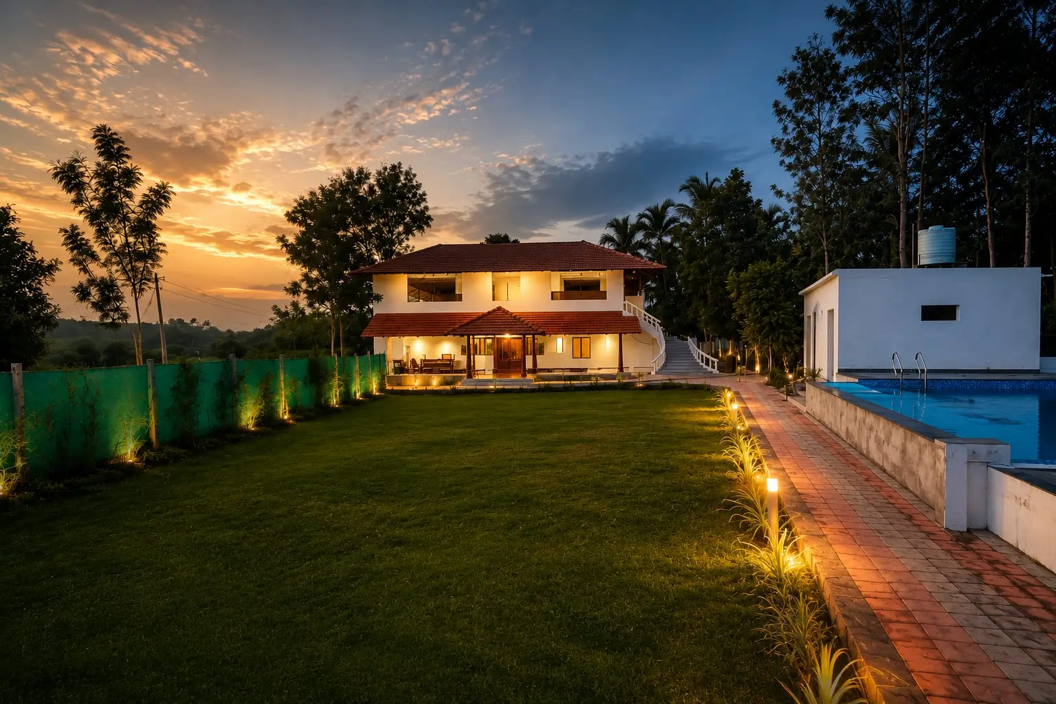 The Wild Retreat villa at dusk, warm lights along the lawn and the swimming pool beyond